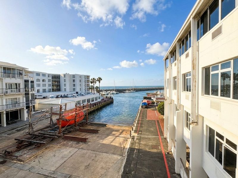 Elevated view overlooking a harbour marina with a concrete slipway, surrounding commercial buildings, and direct access to the ocean.