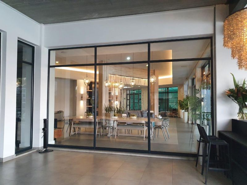 A modern open-plan living and dining area viewed through large floor-to-ceiling glass doors, featuring contemporary lighting and high-quality finishes.