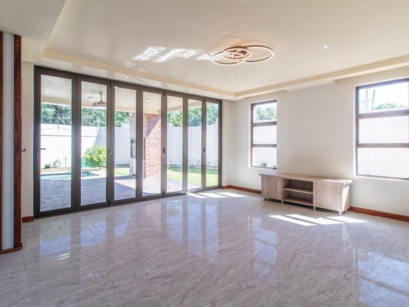 Spacious, light-filled living area featuring large format floor tiles, modern recessed ceiling lighting, and expansive aluminium stacker doors opening to the outdoor patio.