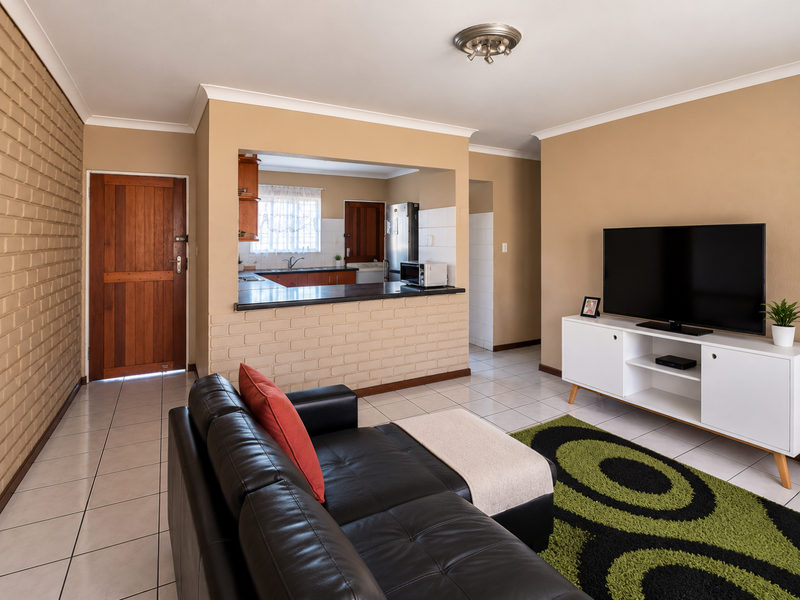 An open-plan living area featuring a brick accent wall, tiled floors, and a pass-through kitchen counter, creating a functional and connected living space.