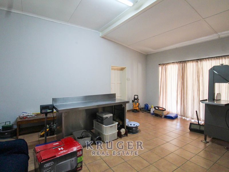 A functional utility space featuring tiled flooring, a suspended ceiling, and a stainless steel prep table, suitable for various workshop or storage purposes.