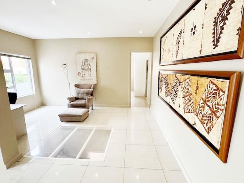 A bright and spacious living area featuring neutral tiled flooring, recessed downlighting, and large aluminium-framed windows.