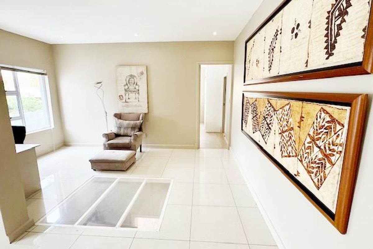 A bright and spacious living area featuring neutral tiled flooring, recessed downlighting, and large aluminium-framed windows.