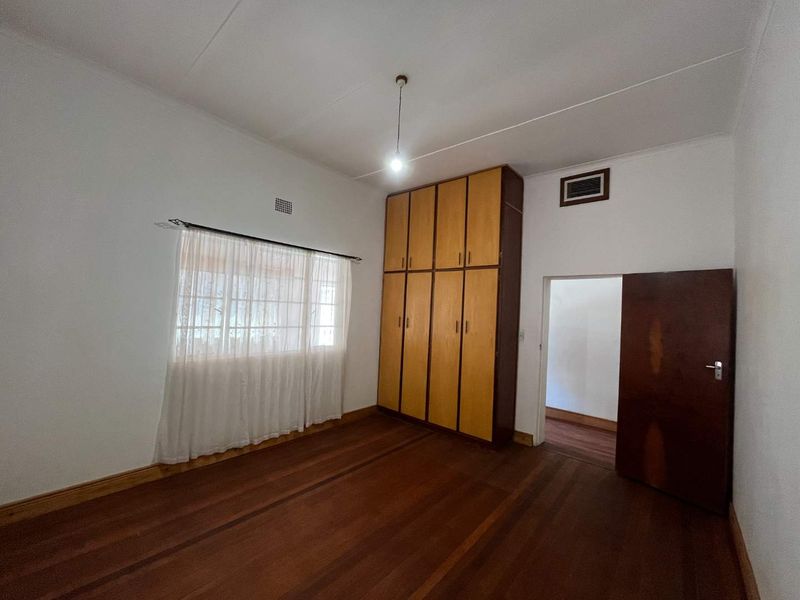 A spacious bedroom featuring original hardwood flooring, built-in wooden cupboards, and a neutral interior finish, offering a blank canvas for potential updates.