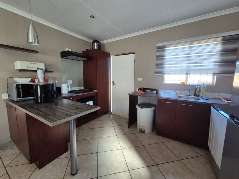A functional kitchen featuring dark wood cabinetry, laminate countertops, a built-in oven and hob, and tiled flooring with natural light from a window.