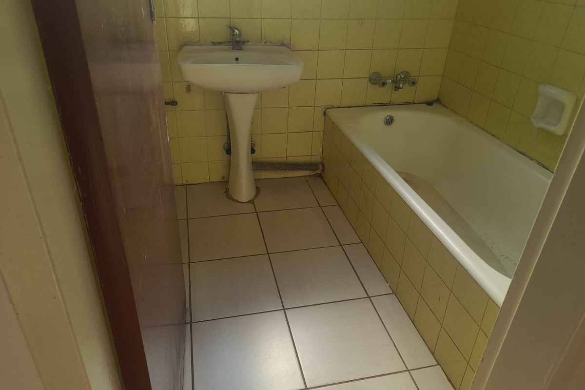 A dated bathroom featuring a pedestal basin, bathtub, and yellow wall tiling, requiring modernization and cosmetic updates to improve its overall condition.
