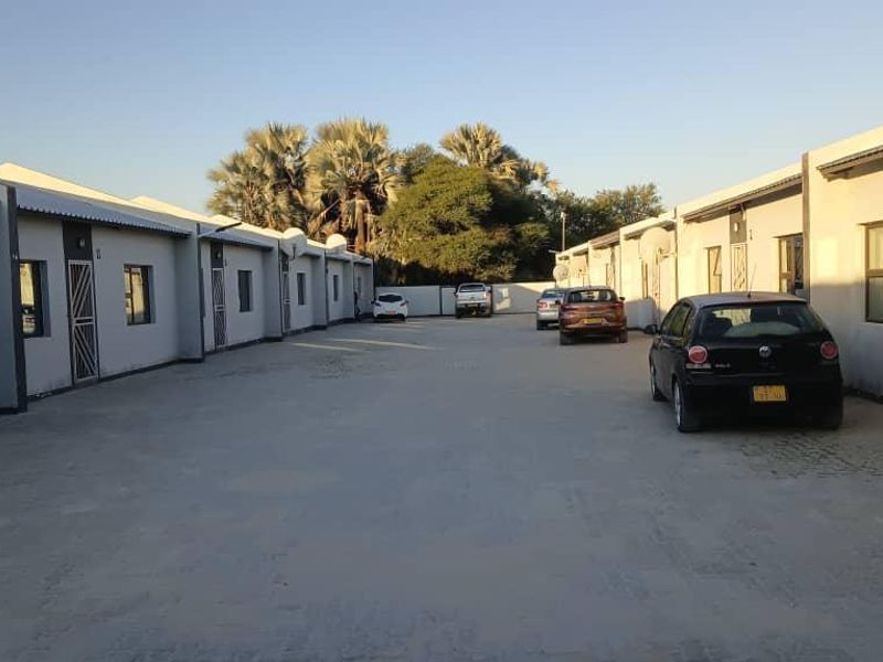 Exterior view of a business complex featuring a central concrete driveway flanked by multiple unit entrances with security gates.