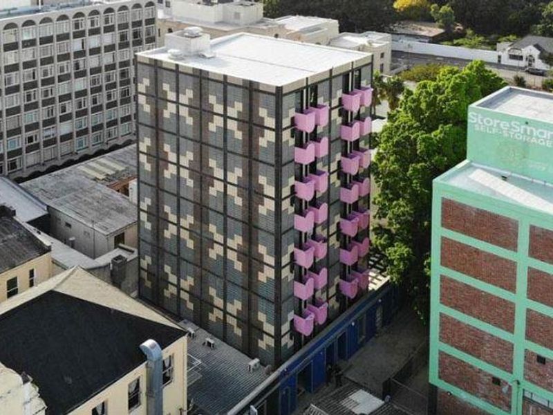 Aerial view of a modern apartment building featuring a distinctive patterned facade and pink balconies, situated in an urban environment.