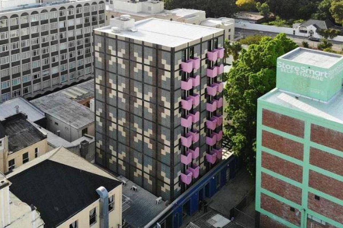 Aerial view of a modern apartment building featuring a distinctive patterned facade and pink balconies, situated in an urban environment.