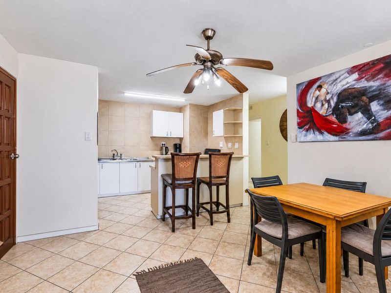 Open plan living and dining area featuring a functional kitchen with breakfast bar, tiled flooring, and a central ceiling fan.