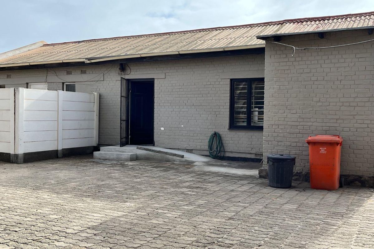 Exterior view of a business property featuring a paved courtyard, brick facade, security gate, and corrugated metal roofing.