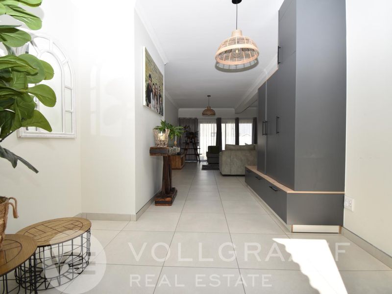 An open-plan living area featuring modern grey built-in cabinetry, neutral tiled flooring, and contemporary pendant lighting, creating a bright and cohesive space.