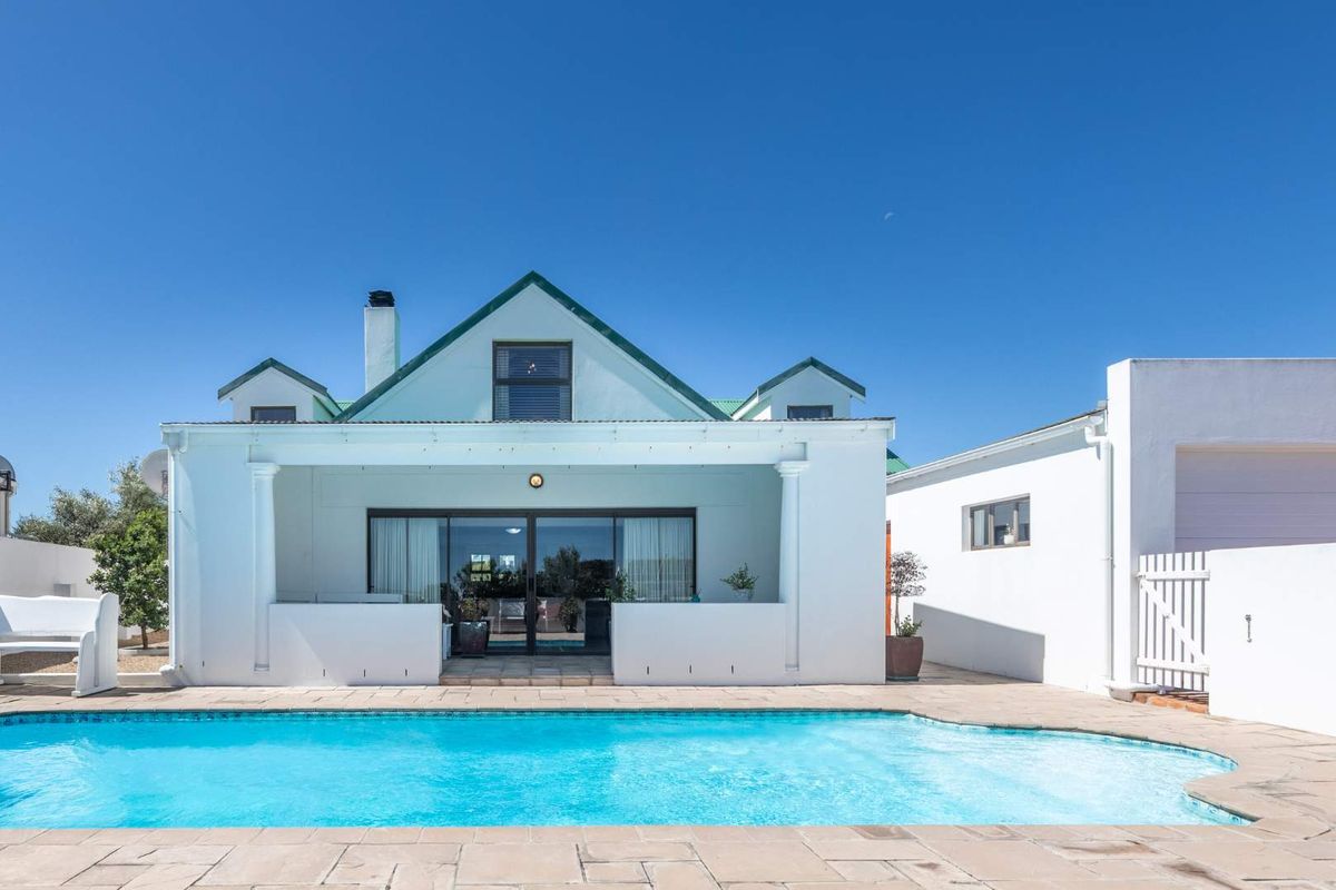 Rear view of the property featuring a swimming pool, paved deck, and a covered patio area with sliding glass doors leading into the home.