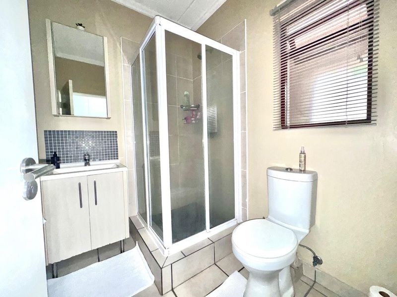 A functional bathroom featuring a corner shower enclosure, vanity cabinet with basin, toilet, and tiled splashback, finished with neutral wall tones.