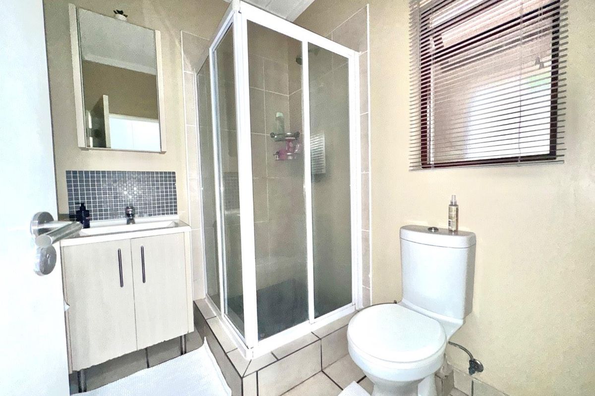 A functional bathroom featuring a corner shower enclosure, vanity cabinet with basin, toilet, and tiled splashback, finished with neutral wall tones.