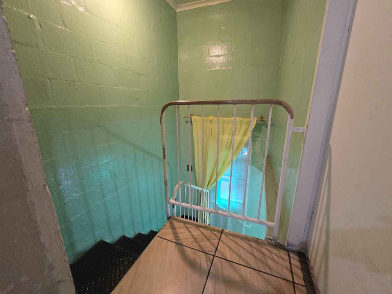A functional stairwell landing featuring painted blockwork walls, tiled flooring, and a metal safety gate leading to the lower level.