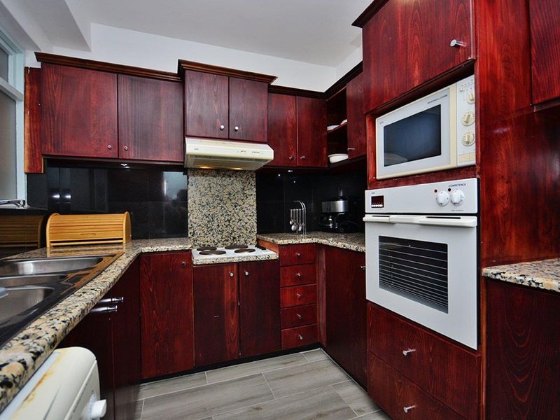 A functional kitchen featuring dark wood cabinetry, granite countertops, and integrated appliances including an oven, microwave, and electric hob.