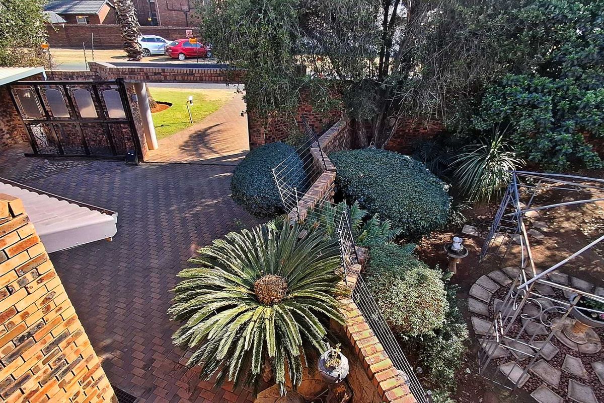 An elevated view of a rear garden featuring brick paving, established landscaping, and secure brick boundary walls with electric fencing.