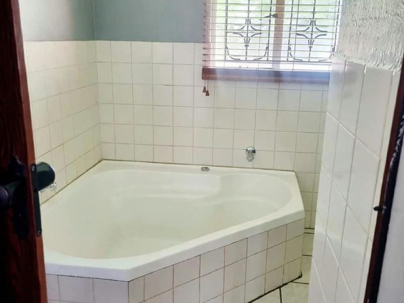 A dated bathroom featuring a corner bathtub with white tiled surround and tiled flooring, requiring cosmetic updates to modernize the space.