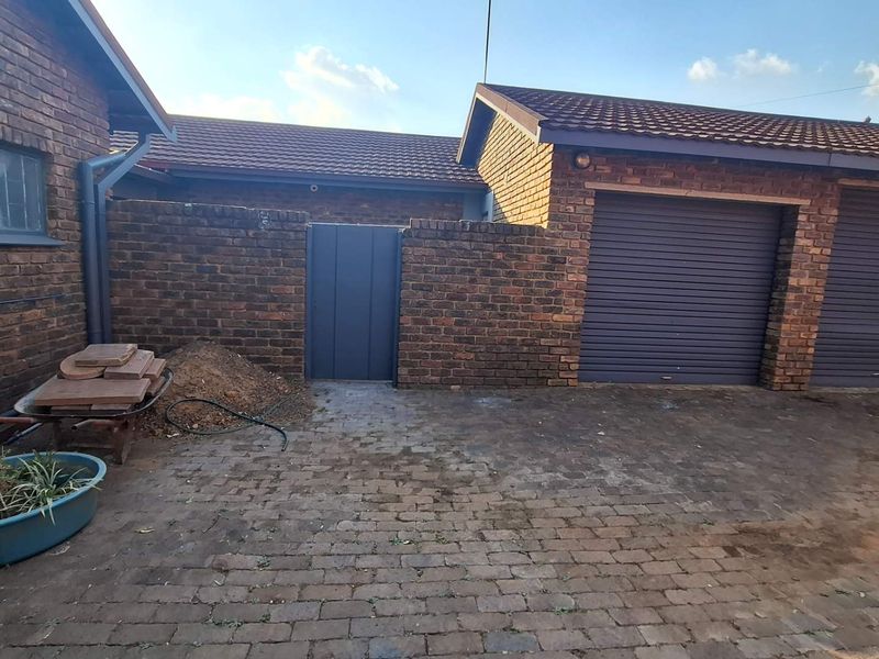 Exterior view of a face brick house featuring a double garage with roller shutter doors and a paved driveway area.