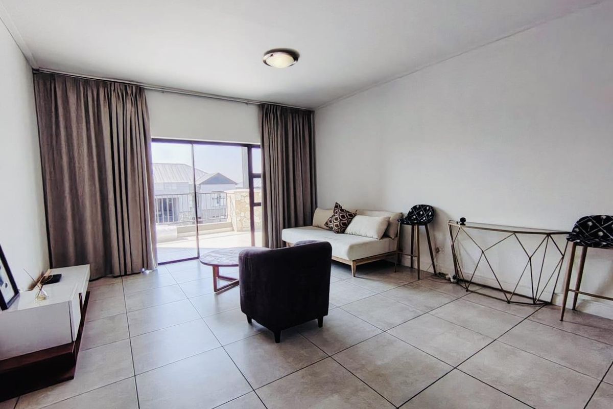A living room featuring large format floor tiles and a sliding glass door providing access to an outdoor balcony area.