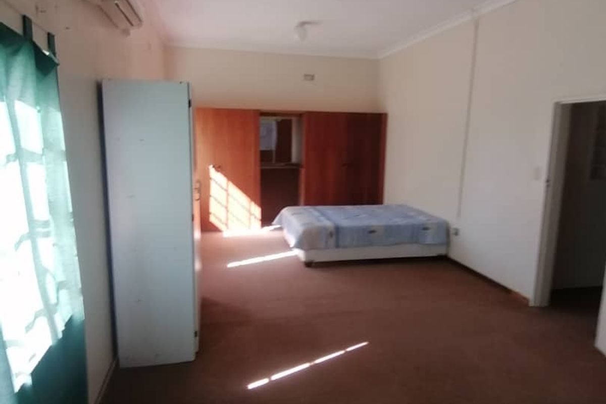 A spacious bedroom featuring built-in wooden cabinetry, wall-mounted air conditioning unit, and carpeted flooring.