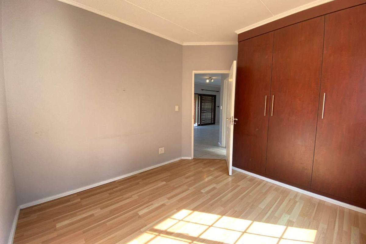 A bright, empty bedroom featuring light-toned laminate flooring and a large, built-in wooden wardrobe with ample storage space.