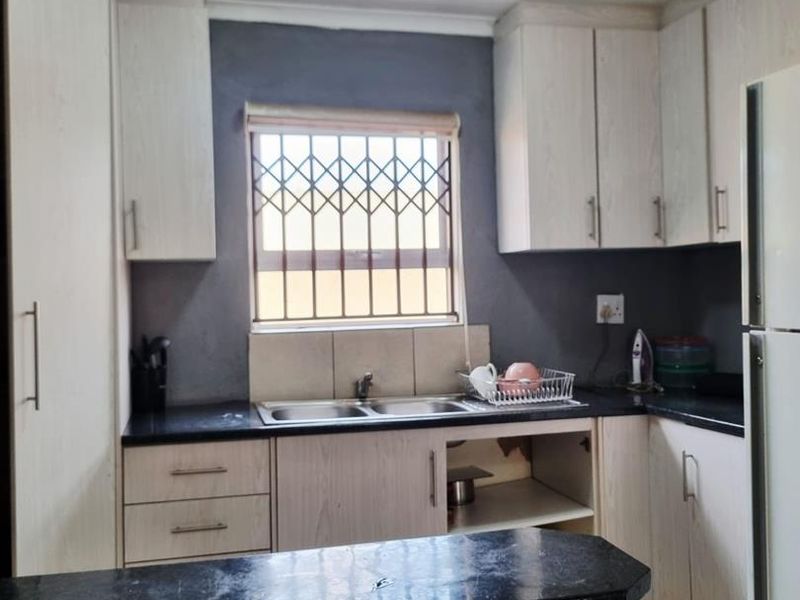 A compact kitchen featuring light wood-finish cabinetry, granite countertops, a breakfast bar, and a double sink with a security-grilled window.
