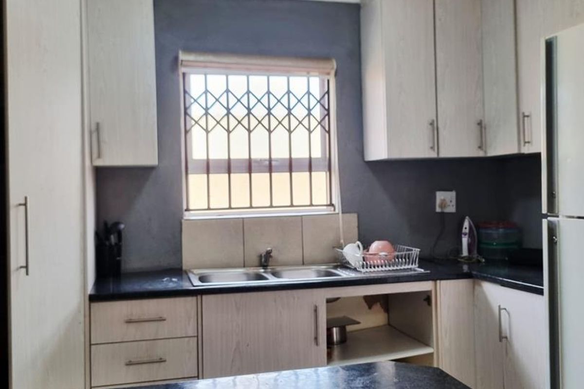 A compact kitchen featuring light wood-finish cabinetry, granite countertops, a breakfast bar, and a double sink with a security-grilled window.