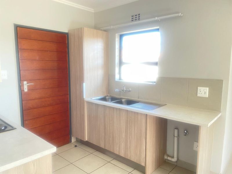 A clean and functional scullery area featuring light wood-look cabinetry, a double sink, tiled splashback, and dedicated plumbing connections for appliances.