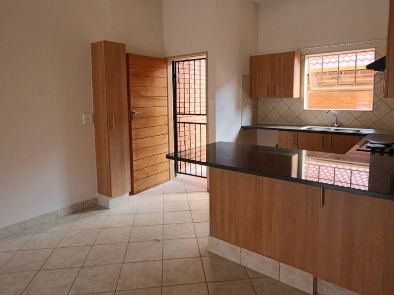 A functional kitchen featuring wood-finish cabinetry, granite countertops, a built-in hob, and tiled flooring, with direct access to an exterior area.