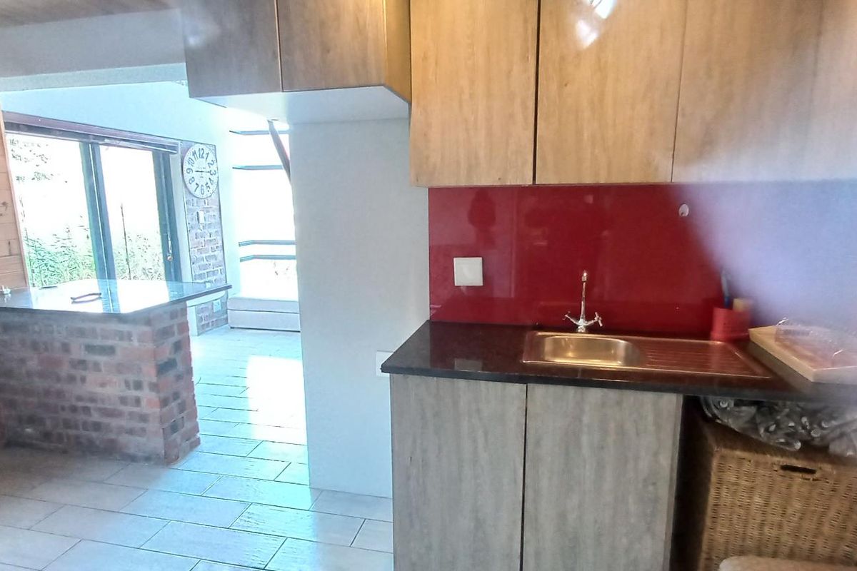 A compact kitchen area featuring granite countertops, a stainless steel sink, and wood-look cabinetry, opening into a living space with brick accents.