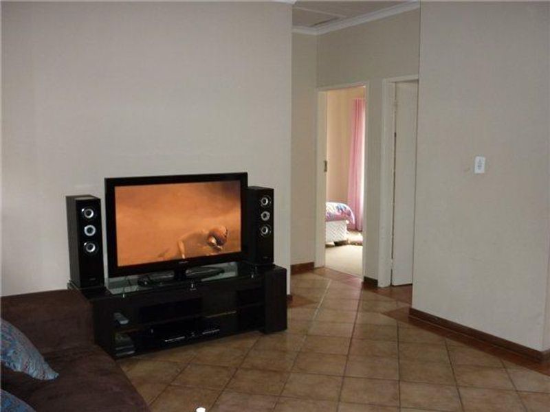A living room area featuring tiled flooring and neutral wall finishes, providing access to adjacent rooms through internal doorways.