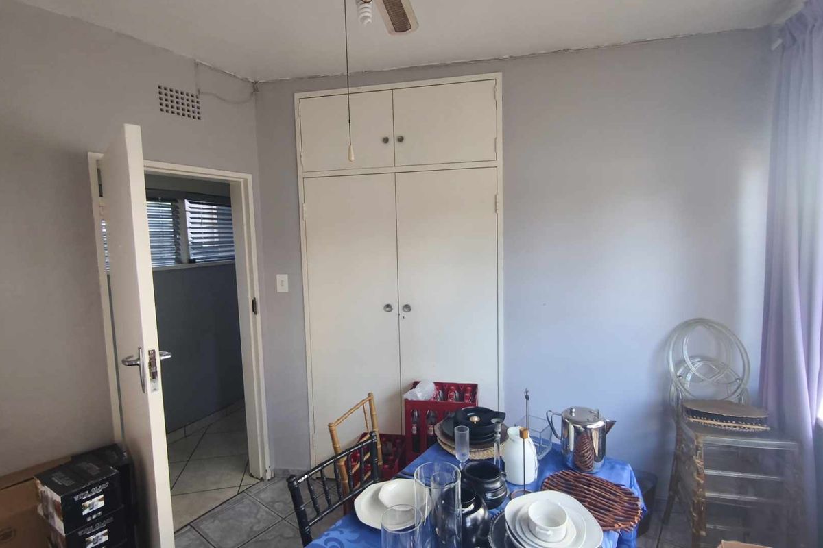 A bedroom featuring built-in cupboards, tiled flooring, and a ceiling fan, providing a functional space with direct access to an adjacent room.