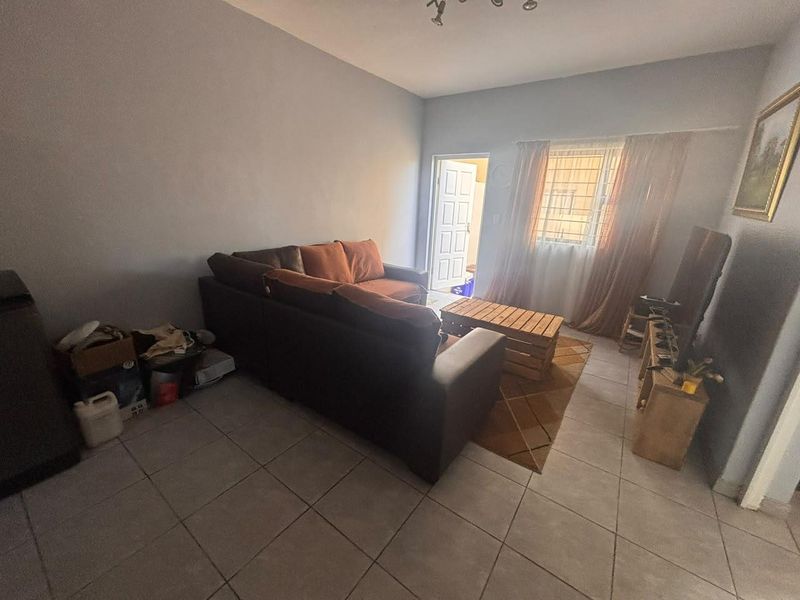 A living room featuring tiled flooring, a window with security bars, and access to an external door.