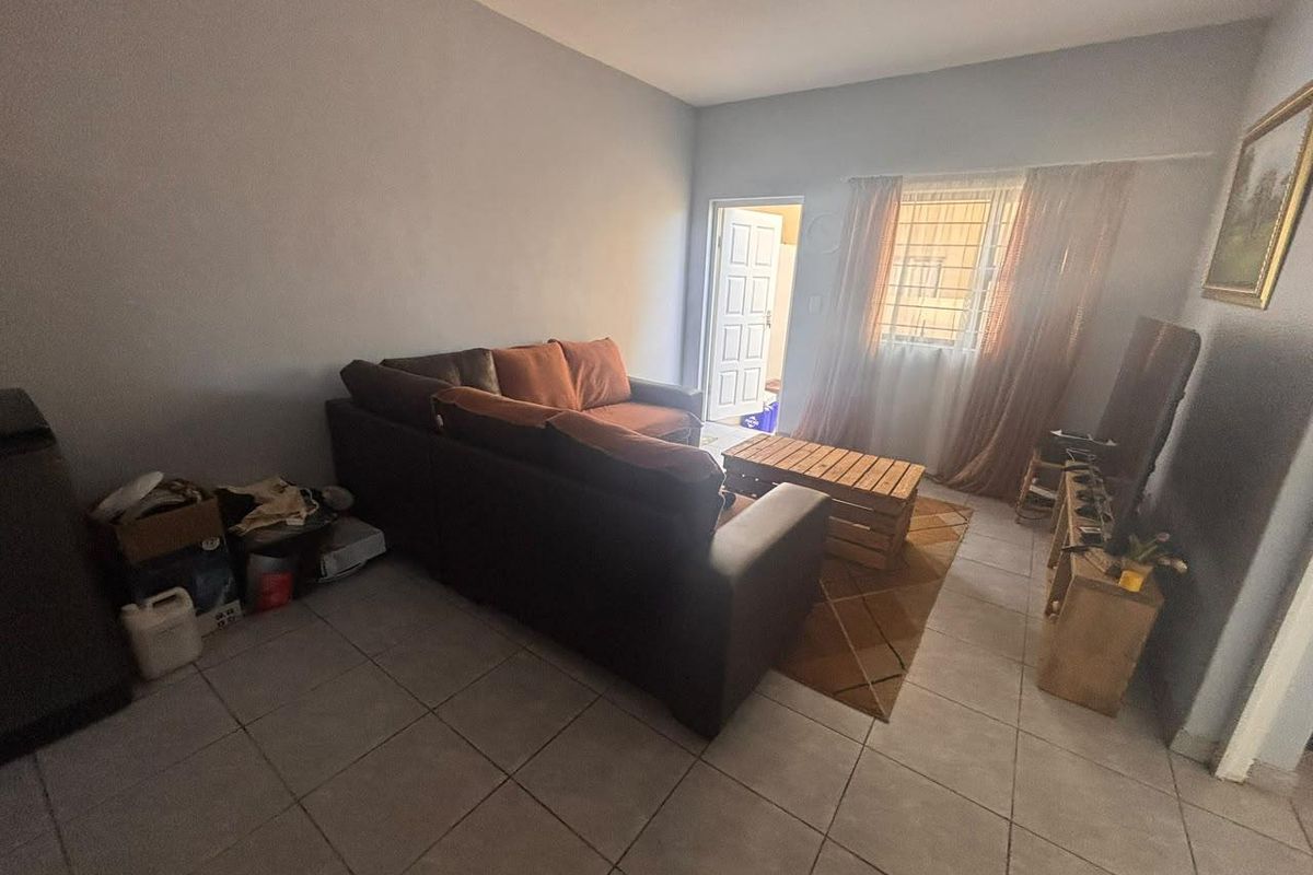 A living room featuring tiled flooring, a window with security bars, and access to an external door.