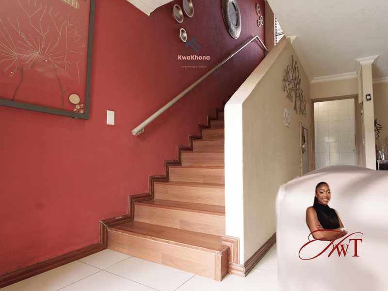 A hallway featuring a staircase with a handrail, tiled flooring, and painted walls, providing access to the upper level of the townhouse.
