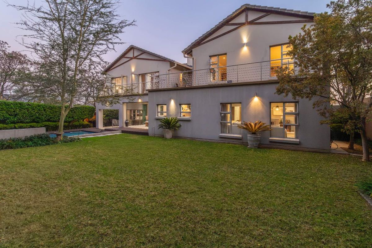 A well-maintained double-story rear elevation featuring a spacious lawn, swimming pool, and an upper-level balcony with stainless steel balustrades.