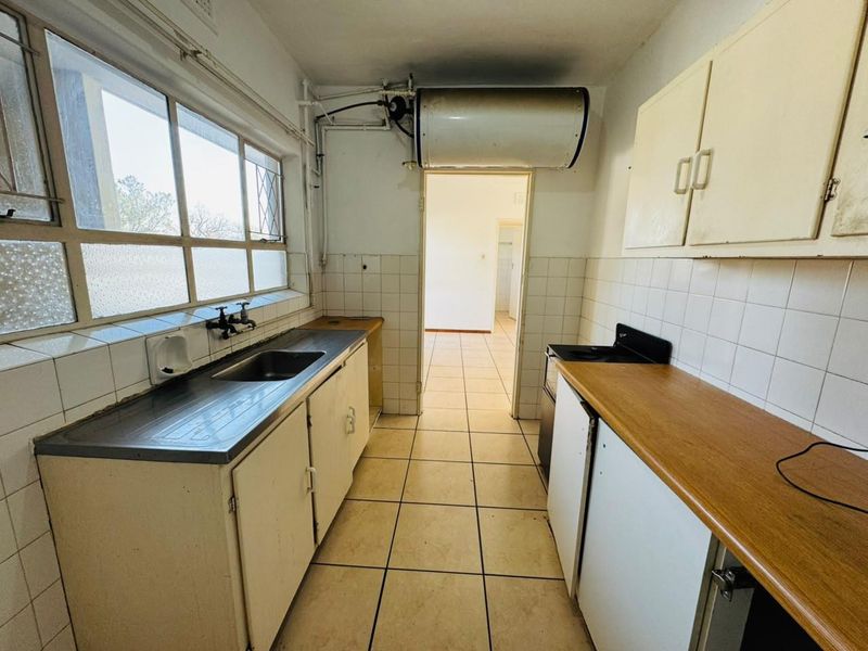 A dated kitchen featuring original cabinetry, tiled splashbacks, and a stainless steel sink, offering significant potential for a modern renovation and layout update.