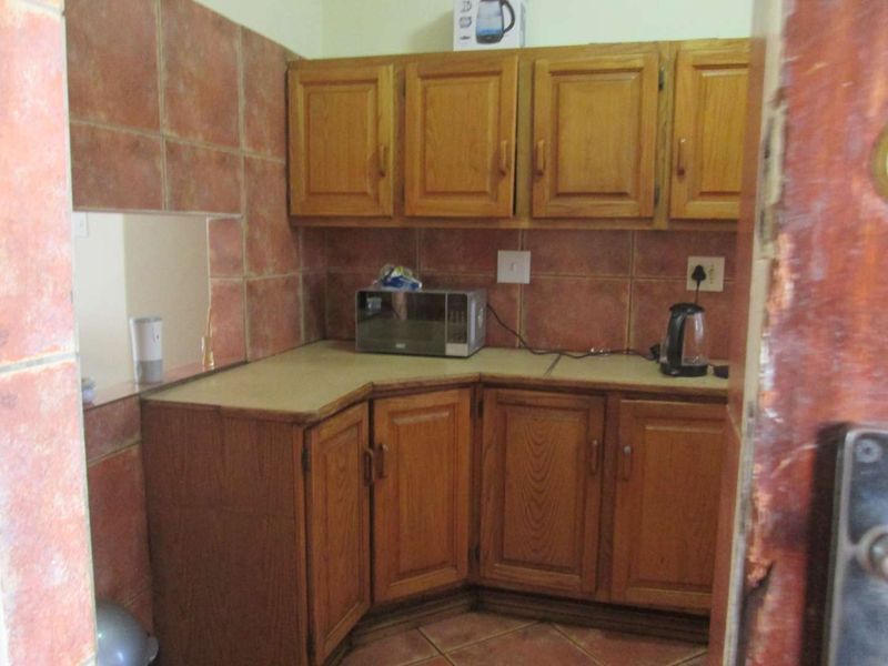 A compact kitchen featuring traditional wooden cabinetry, tiled backsplash, and laminate countertops, requiring cosmetic updates to modernize the space.
