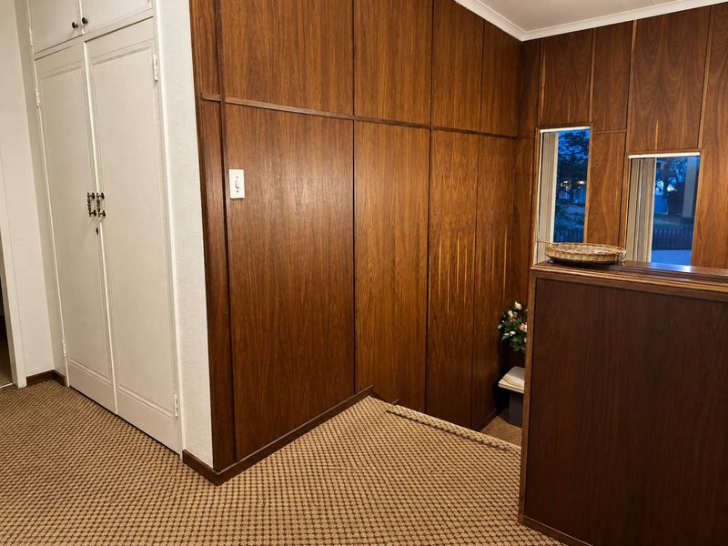 A hallway featuring dated wood paneling, built-in storage cabinetry, and carpeted flooring.