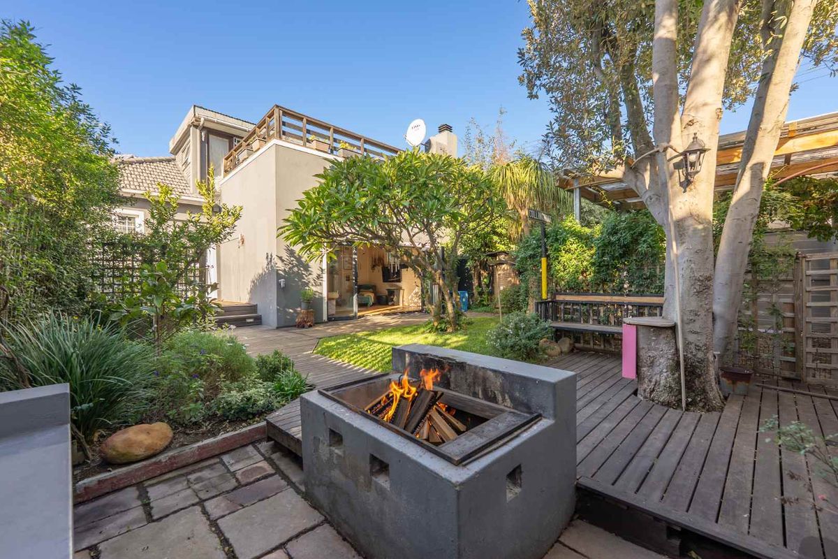 Rear garden featuring a built-in fire pit, timber decking, paved patio area, and an elevated balcony overlooking the landscaped outdoor space.
