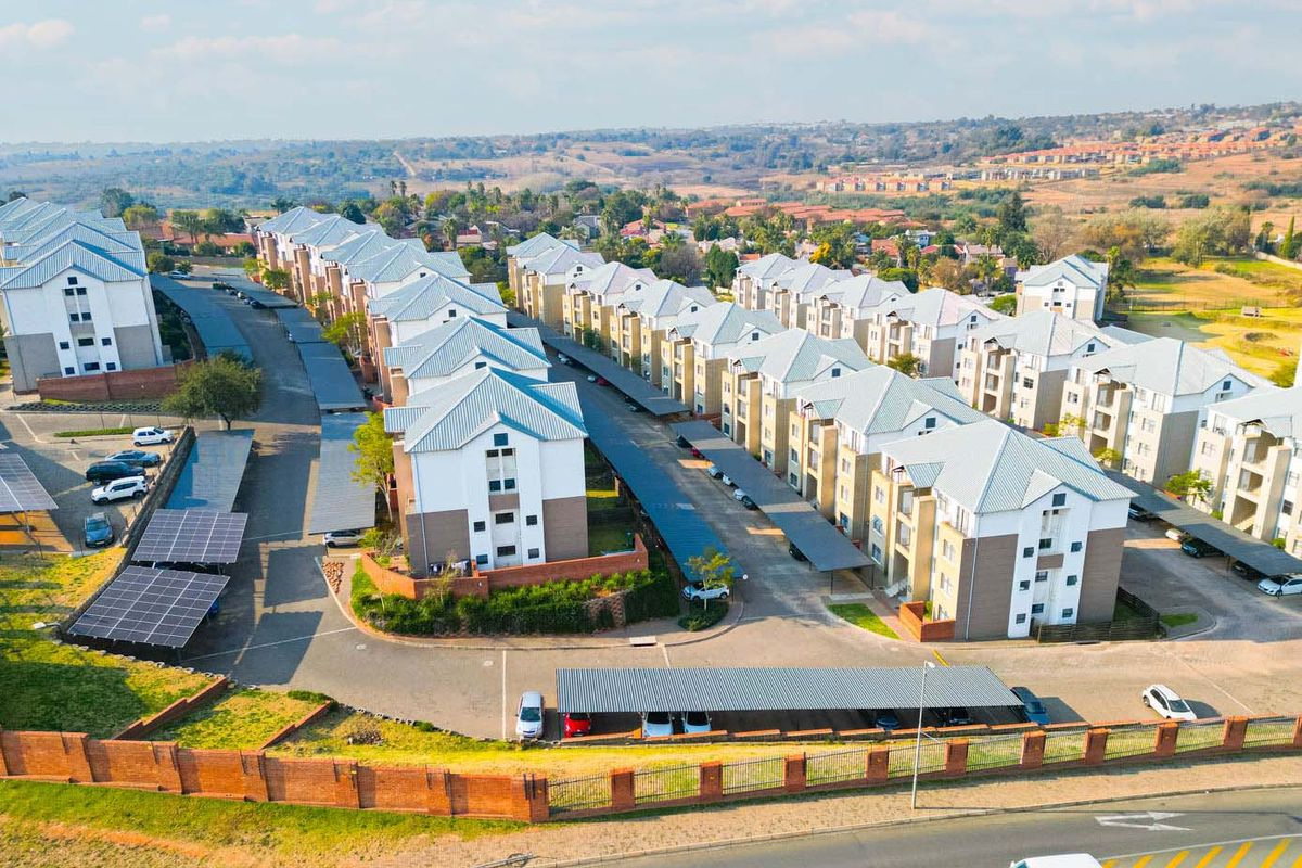 Aerial view of a modern apartment complex featuring multiple residential blocks, covered parking bays, solar panel installations, and well-maintained surrounding grounds.