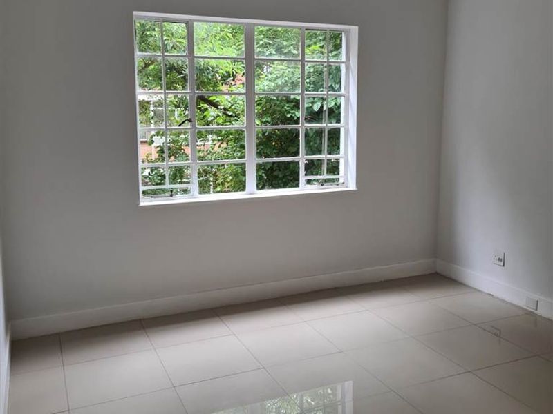 A bright, empty bedroom featuring neutral tiled flooring and a large multi-pane window overlooking greenery.