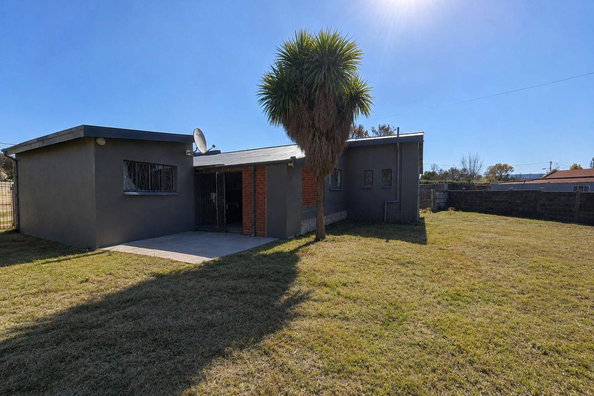 Rear view of the property featuring a concrete patio area, brick and rendered exterior walls, and a spacious backyard with perimeter fencing.