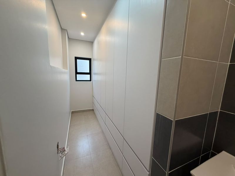A clean, modern dressing area or bedroom space featuring extensive built-in cabinetry, neutral tiled flooring, and recessed lighting.