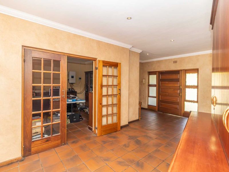 Spacious entrance hall featuring terracotta floor tiles, warm-toned walls, and classic wooden french doors leading into an adjacent room.