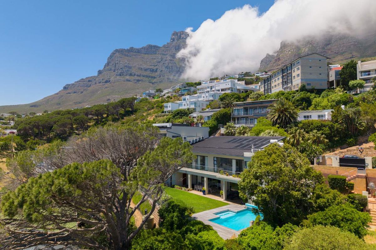 Aerial view of a residential property featuring a swimming pool, landscaped garden, and solar panels, set against a scenic mountain backdrop.