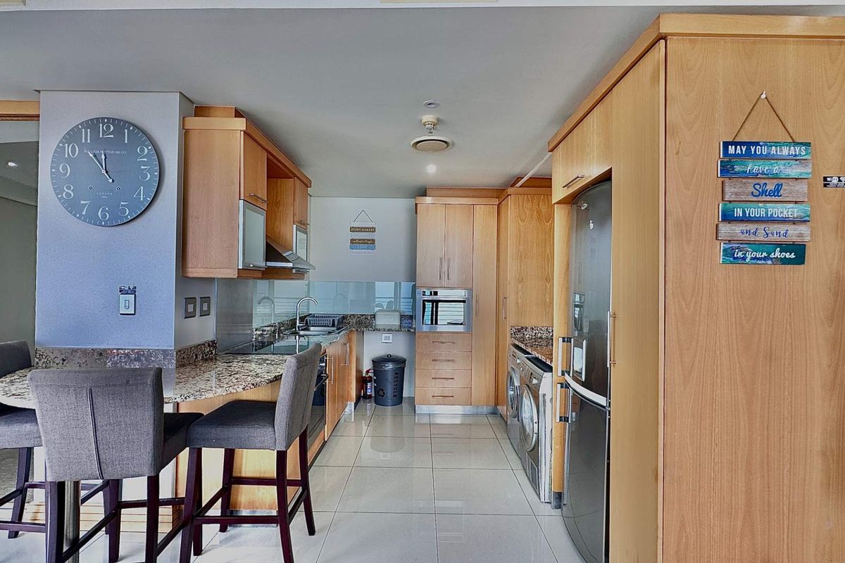 A functional kitchen featuring light wood cabinetry, granite countertops, a breakfast bar, and integrated appliances, finished with neutral floor tiles.