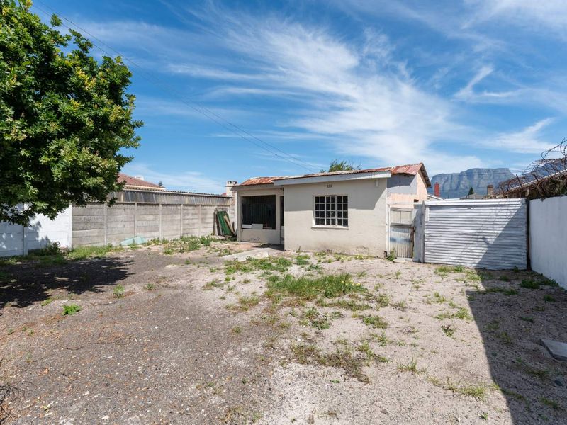Rear exterior view of the property featuring a small structure with a corrugated roof, enclosed by concrete boundary walls and security fencing.